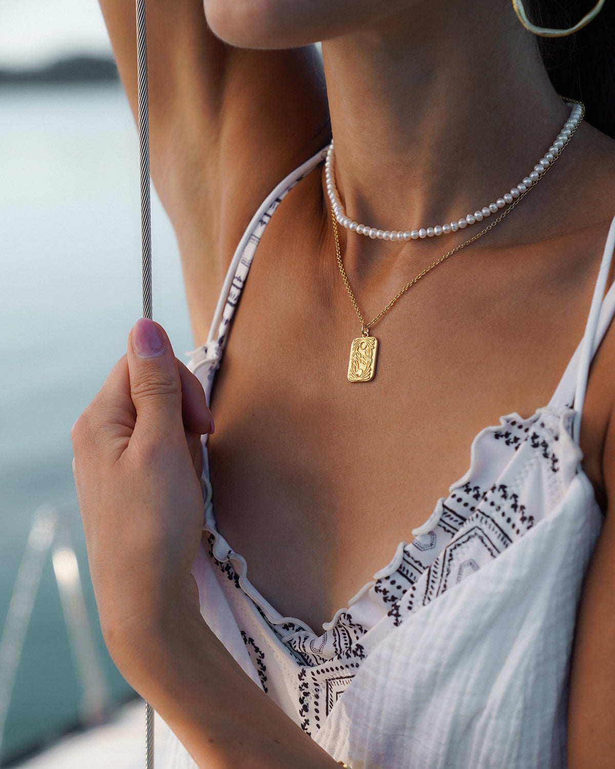 der Oberkörper einer Frau mit Gold Halskette und Perlenkette um den Hals. im Hintergrund sieht man das Meer.