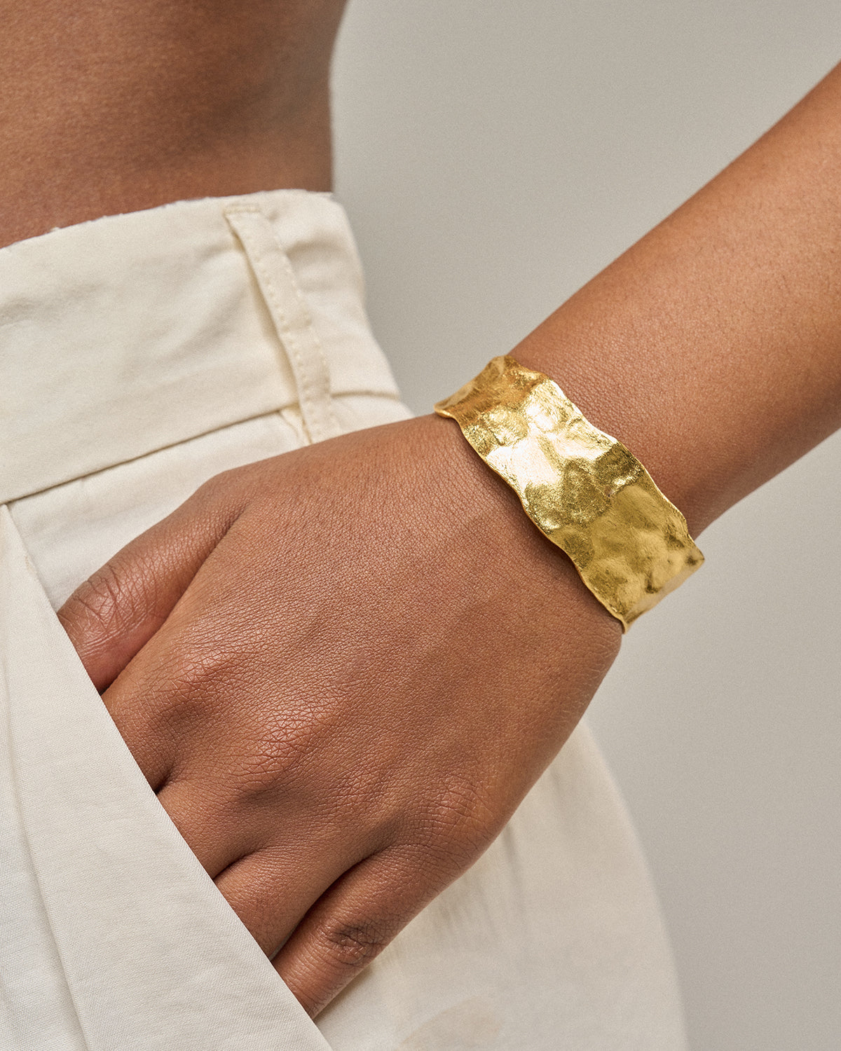 eine Hand einer Frau mit einem goldenen Armreif an ihrem Handgelenk.