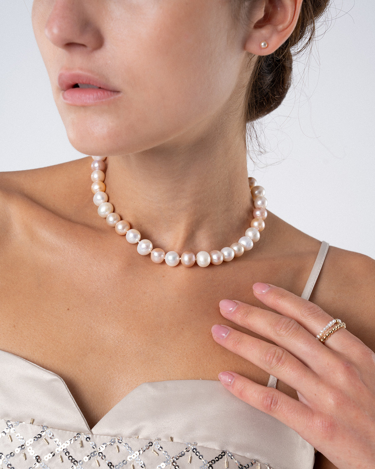 Frau trägt eine Perlenkette für Damen mit schimmernden Süßwasserperlen in Weiß- und Rosétönen zu einem eleganten, hellen Kleid.