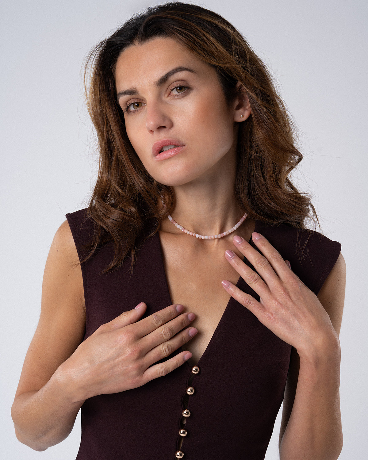 Frau mit schulterlangem braunem Haar trägt eine zarte rosa Opal Choker zu einem ärmellosen, dunklen Kleid vor hellem Hintergrund.
