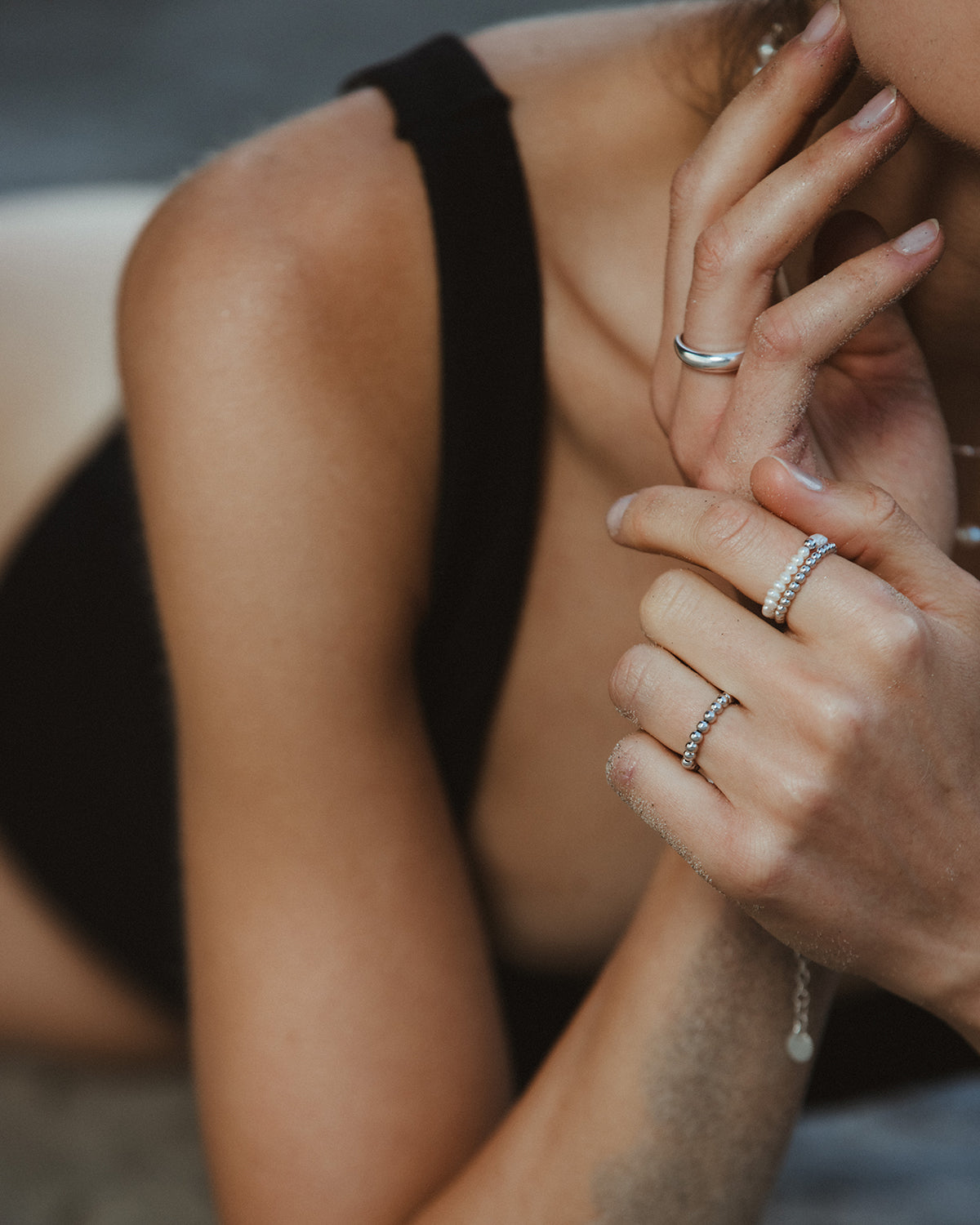 Nahaufnahme einer Frau mit schwarzen Trägern, die mehrere Ringe trägt, darunter ein filigraner Perlenring aus kleinen weißen Süßwasserperlen und feine Silberringe, kombiniert im modernen Ring-Stacking-Look.