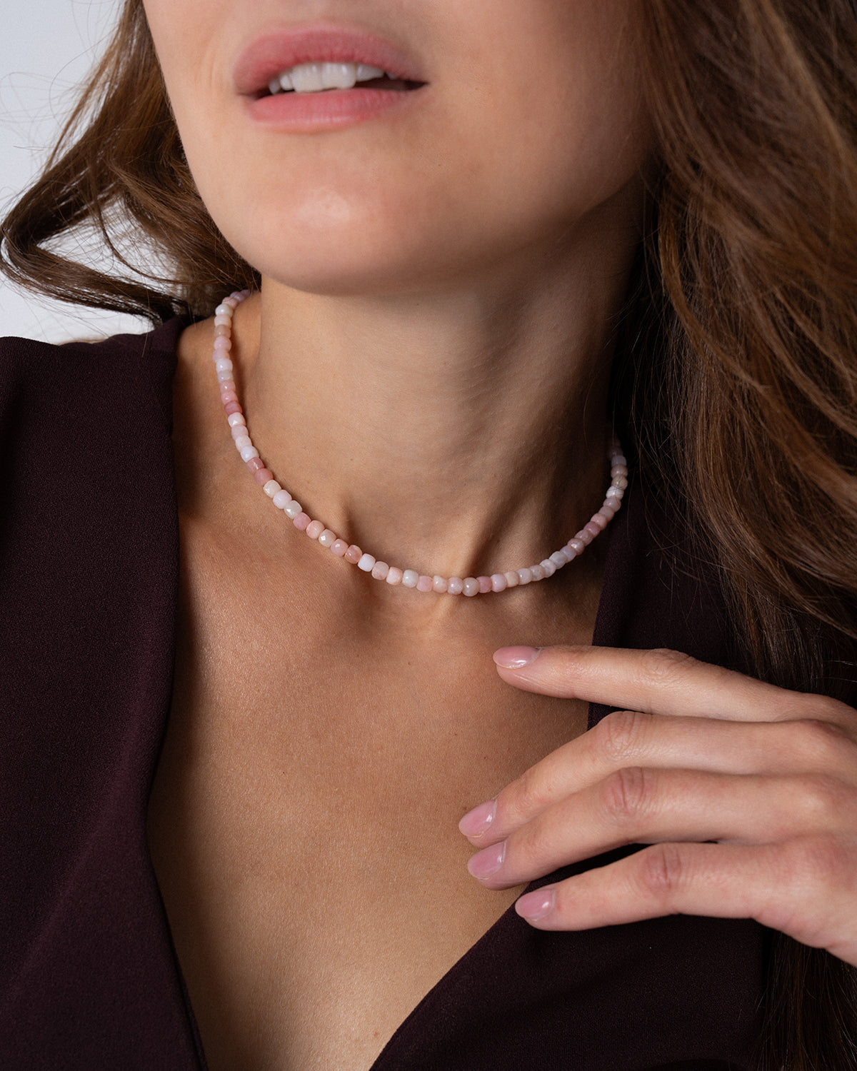 Detailaufnahme einer rosa Opal Halskette mit facettierten Perlen in zarten Rosatönen, getragen als Choker am Hals einer Frau mit dunklem ärmellosem Kleid.