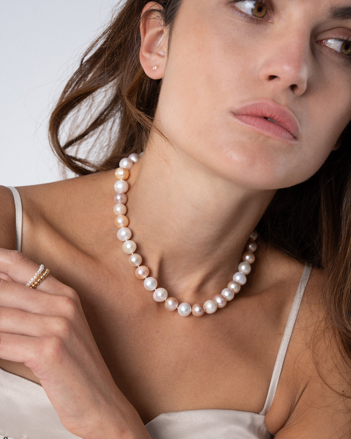 Porträt einer Frau mit braunen Haaren, die eine Perlenkette aus schimmernden Süßwasserperlen in Weiß- und zarten Rosétönen zu einem eleganten, hellen Kleid trägt.